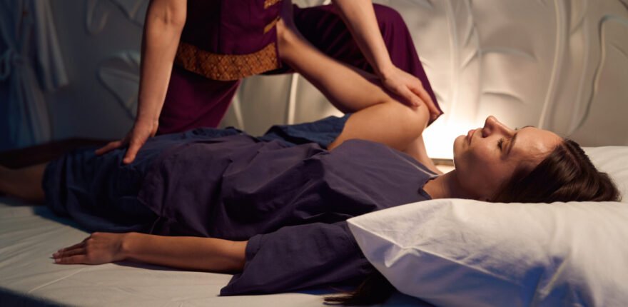Massage therapist bringing bent knee of young woman towards her chest while palm pressing on thigh of other leg